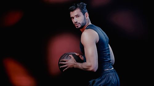 bearded sportsman playing basketball on dark background