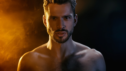 Portrait of bearded and muscular sportsman  with smoke on black