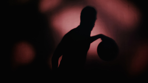 shadow of sportsman playing basketball on dark background