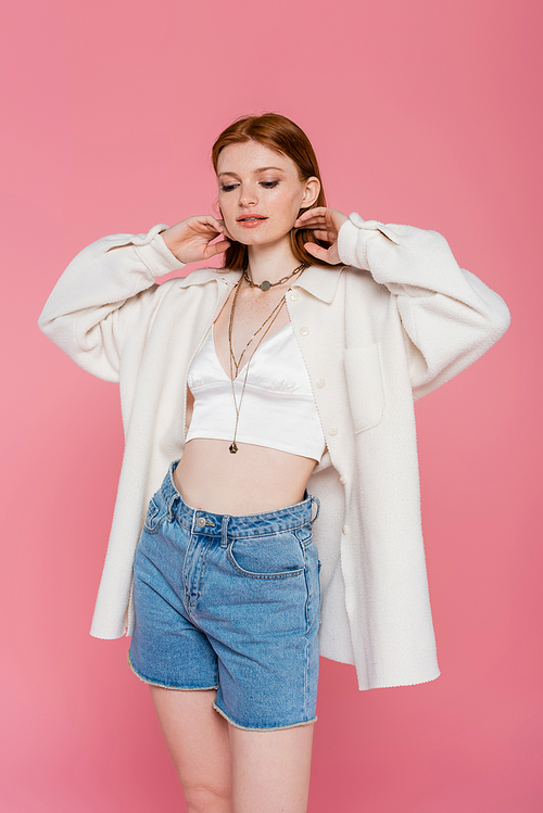 Pretty red haired woman in jacket and denim shirts posing isolated on pink