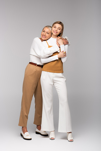 full length of happy middle aged mother hugging young daughter on grey