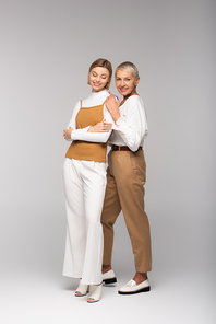 full length of pleased middle aged mother standing with happy young daughter on grey