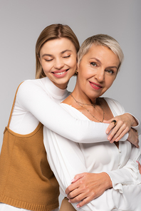 pleased young daughter hugging middle aged mother isolated on grey