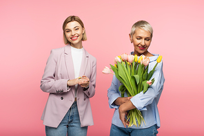 happy middle aged mother holding bouquet of tulips near pleased daughter isolated on pink
