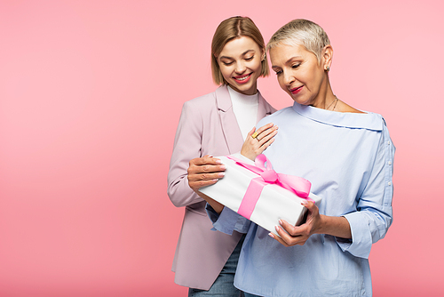happy mature mother holding present near pleased young daughter isolated on pink