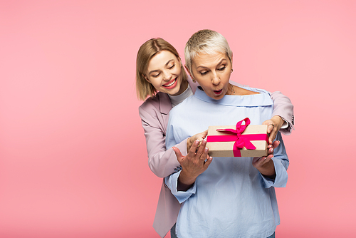 pleased young daughter presenting gift to surprised mother isolated on pink