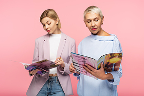 middle aged mother and young daughter reading magazines isolated on pink