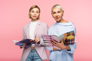 mature mother and young daughter holding magazines isolated on pink