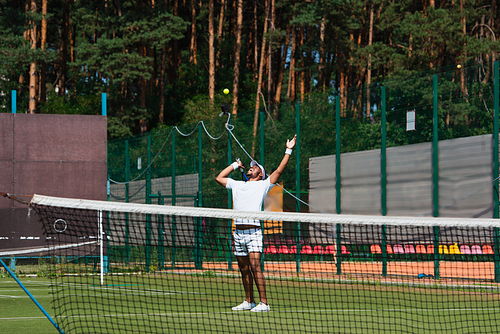 Excited african american sportsman looking at ball near net on tennis court