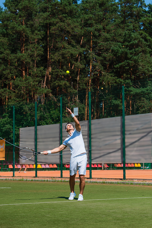Young sportsman with racket throwing ball while playing tennis on court