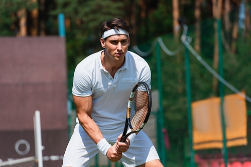 Concentrated sportsman holding tennis racket on court outdoors