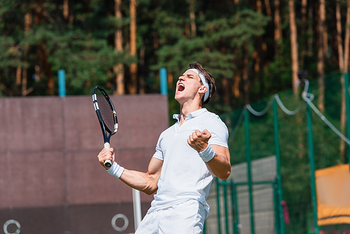 Excited sportsman with tennis racket showing yes gesture on court