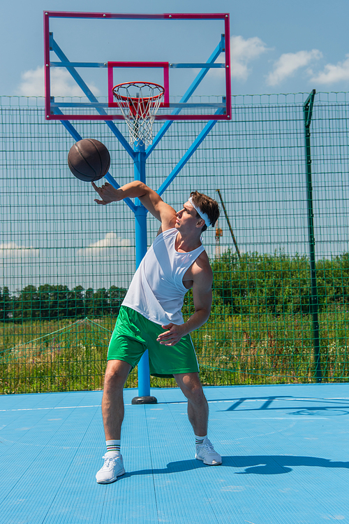 Sportive player spinning basketball ball on playground