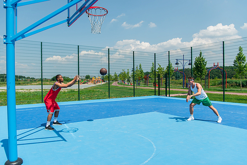 Side view of basketball ball near multiethnic sportsmen on playground
