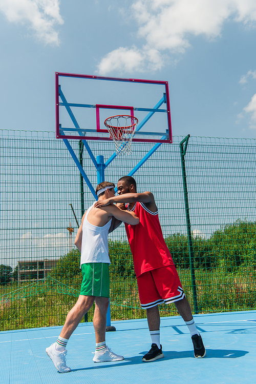 Multiethnic sportsmen hugging on streetball playground