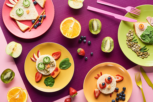 top view of plates with fancy animals made of food near fruits on purple background