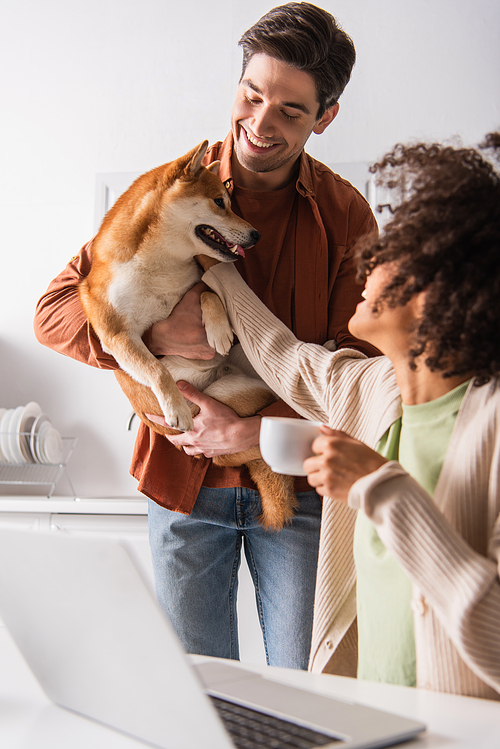 african american woman with coffee cup stroking shiba inu dog in hands of smiling boyfriend