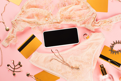 Top view of smartphone with blank screen near lingerie, credit cards and accessories on pink background