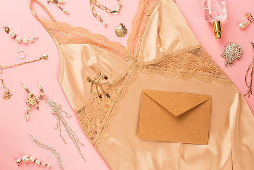 Top view of envelope, golden accessories and camisole on pink background