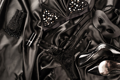 Top view of sexy lingerie, mask and heels on black satin background