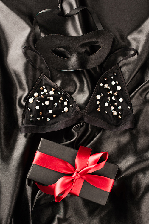 Top view of present near bra and sexual mask on black satin background