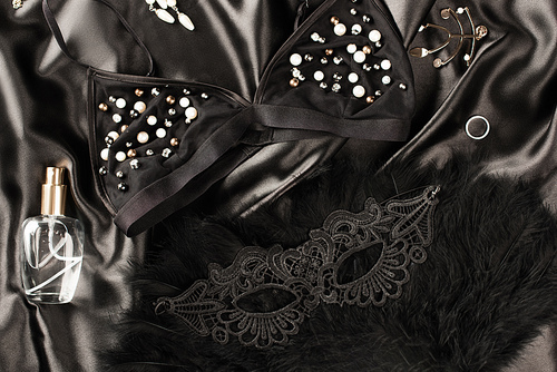 Top view of bra, perfume and sexual mask on black satin background