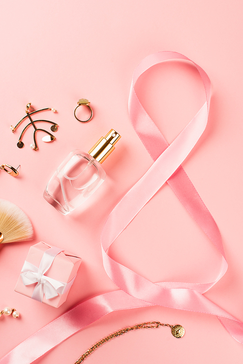 Top view of ribbon in shape of 8 sign near gift, perfume and accessories on pink background