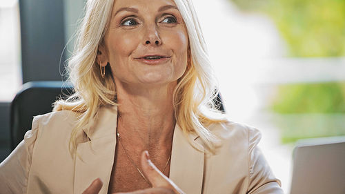 excited middle aged businesswoman looking away while talking in office