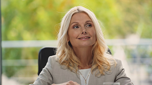 blonde middle aged businesswoman smiling while looking away in office