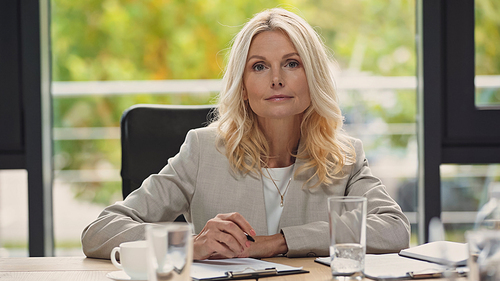 blonde middle aged businesswoman holding pen and  in meeting room