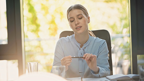 dreamy and positive businesswoman holding pen while sitting in office