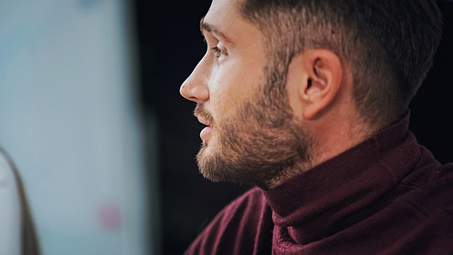 profile of young bearded businessman in turtleneck on blurred background