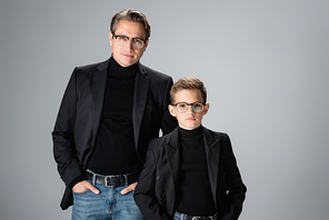 Father and preteen son in eyeglasses and jackets  isolated on grey