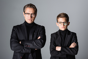 Stylish man and boy in jackets and eyeglasses crossing arms isolated on grey