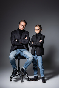 Stylish man posing on chair near son on grey