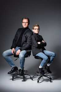 Stylish father and son posing on chairs on grey