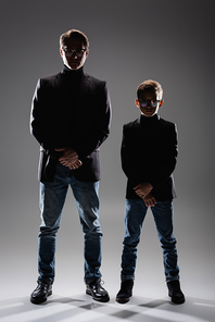Dad and son in jackets and eyeglasses posing on grey