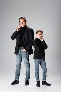 Full length of father and son talking on smartphones on grey background