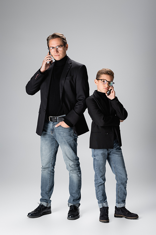 Stylish parent and son talking on cellphones on grey background