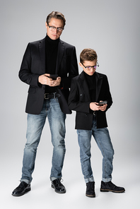 Full length of man and preteen son using smartphones on grey background