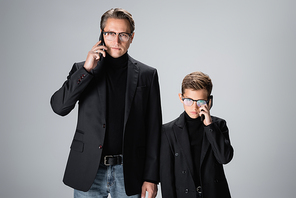 Boy and dad in jackets talking on smartphones isolated on grey