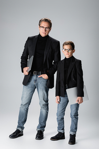 Stylish parent and son holding laptops on grey background