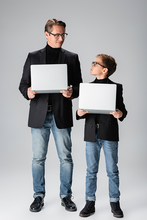 Boy in jacket holding laptop and looking at dad on grey background