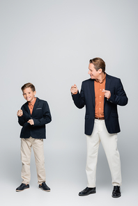 Full length of stylish father and son dancing on grey background