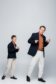 Man and stylish preteen son dancing on grey background