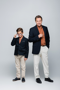 Full length of trendy parent holding eyeglasses near son on grey background