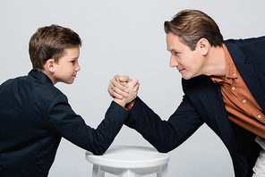 Side view of father and son looking at each other during arm wrestling isolated on grey