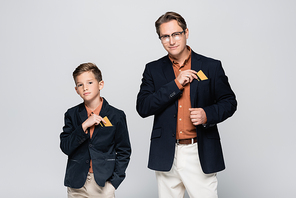 Stylish father and son taking credit cards from pockets of jackets isolated on grey