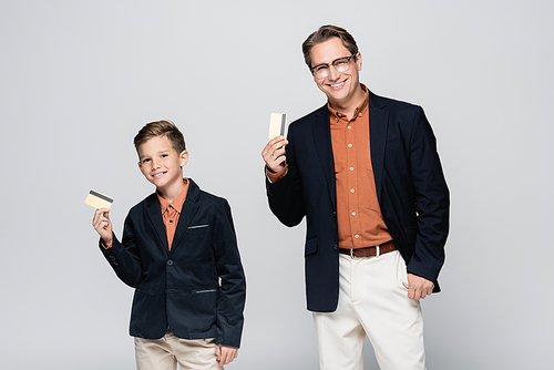 Smiling dad and son holding credit cards isolated on grey