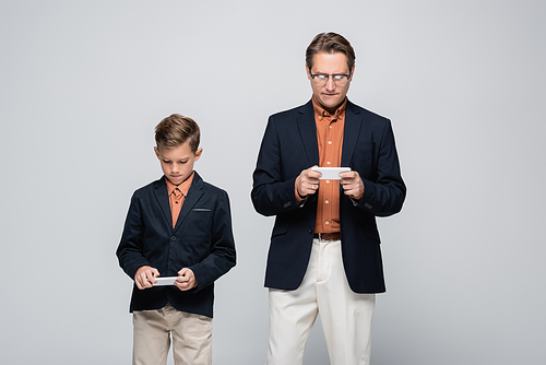 Father and son in jackets using cellphones isolated on grey